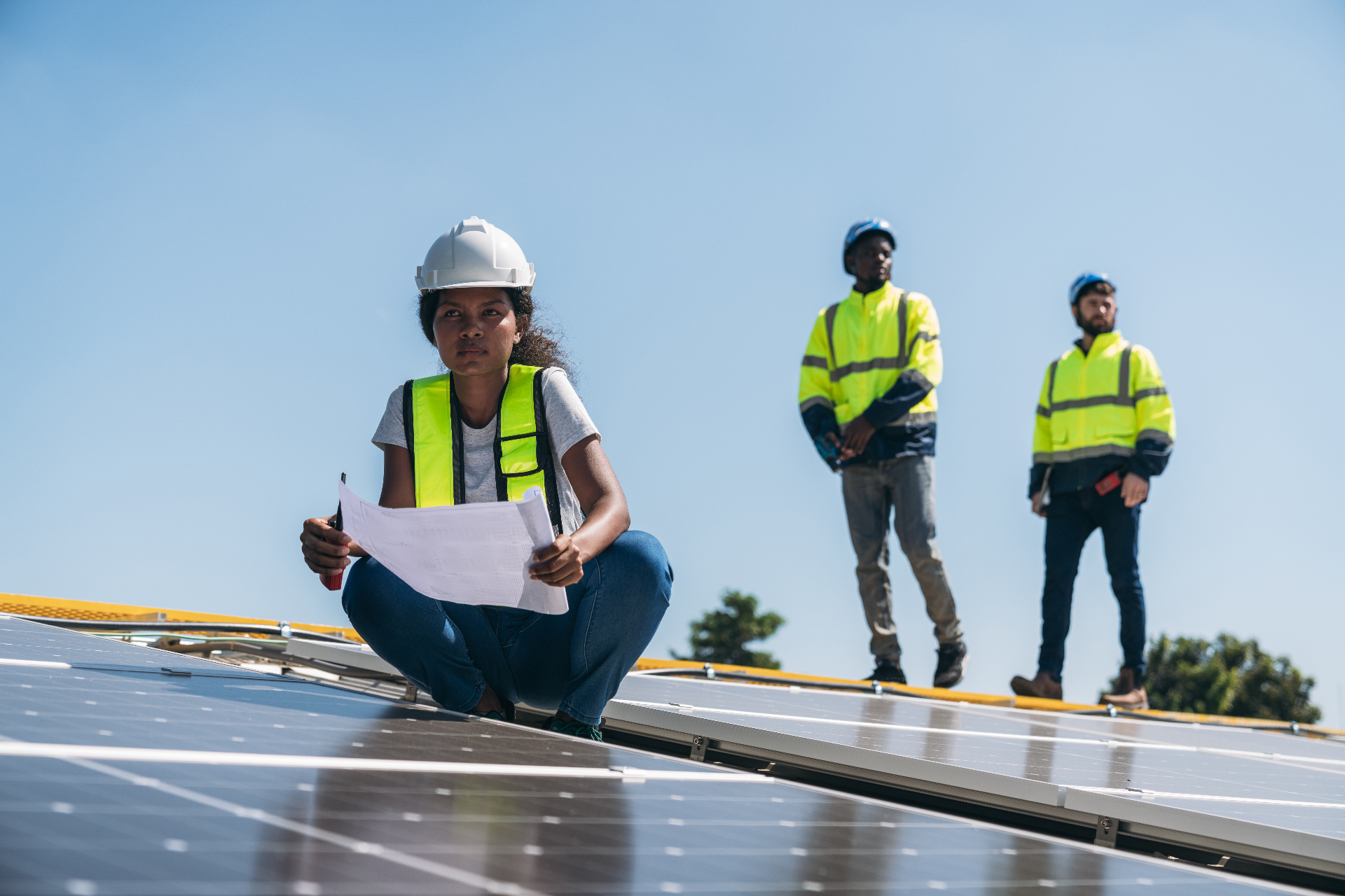 Engineer reviewing plans on a rooftop solar installation while technicians work behind