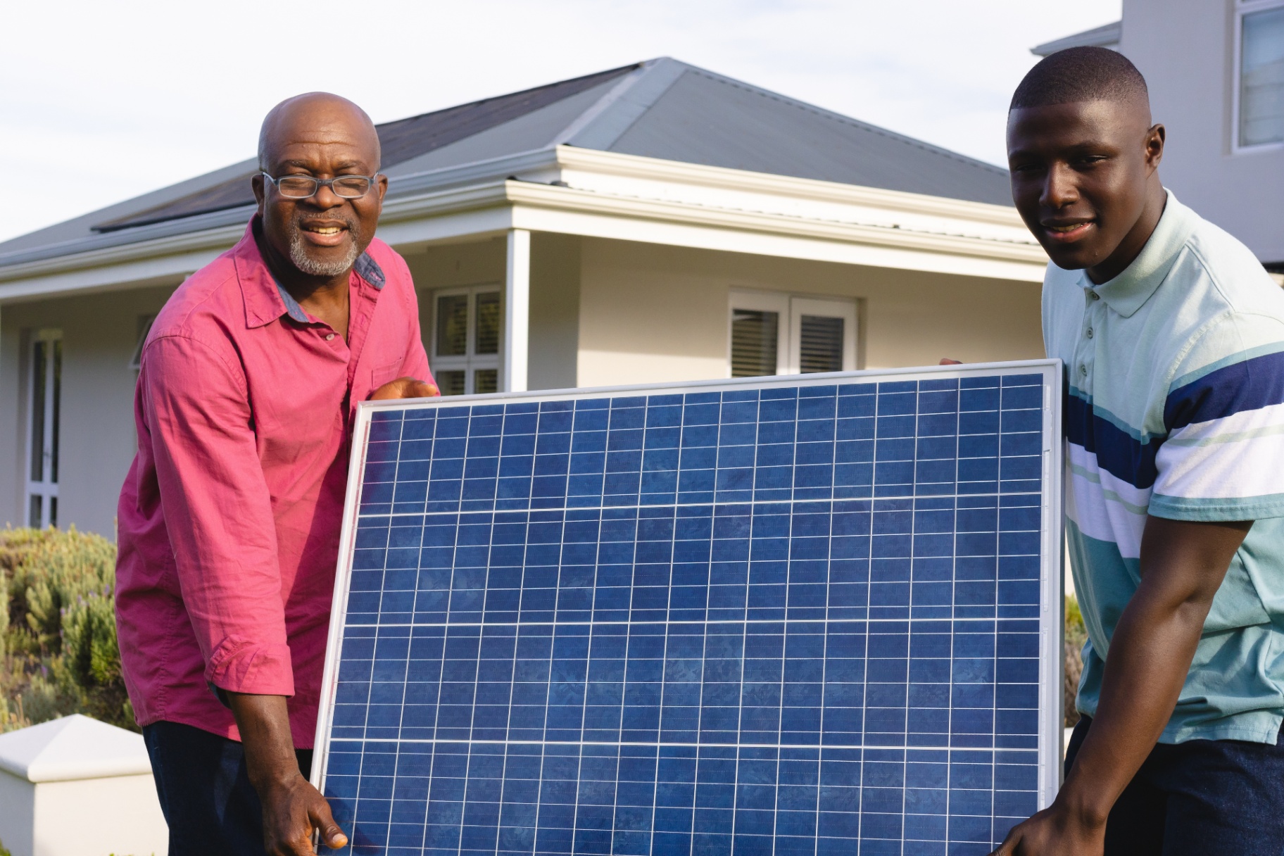 Two installers carrying a residential solar panel in front of a modern home